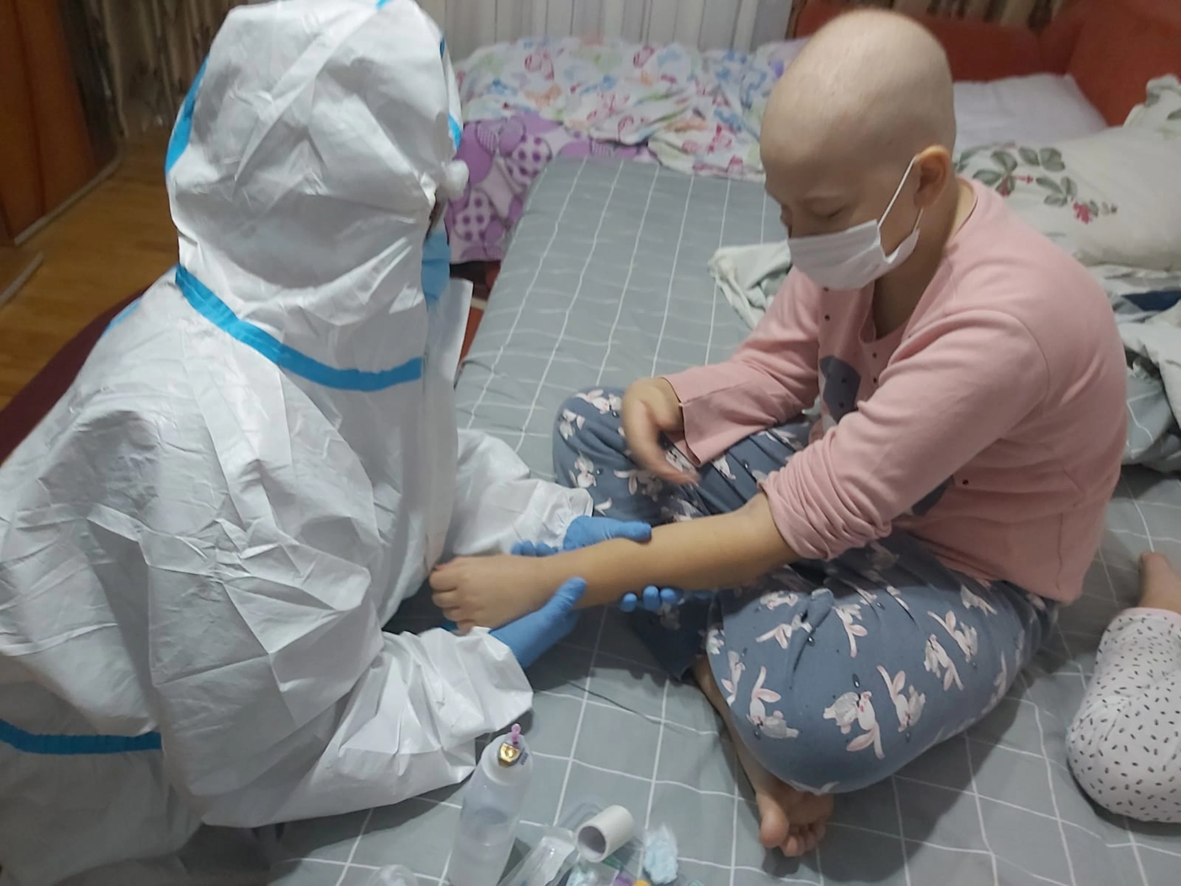 Asistentă în echipament de protecție recoltează o probă de sânge unui copil, acasă